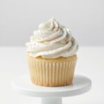 Maczek Cukrowy Srebrny 50g Posypka na Tort Blask i Elegancja › Udanewypieki Biała babeczka cupcake ozdobiona srebrnym maczkiem cukrowym – błyszczące kuleczki na kremie maślanym, dekoracja na wesele lub urodziny