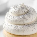 Maczek Srebrny Posypka Cukrowa 50g Dekoracje na Tort Muffinki Ciastka › Udanewypieki Zbliżenie na krem babeczki ozdobiony srebrnym maczkiem cukrowym – drobne błyszczące kuleczki posypki cukrowej na białym kremie