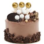 1fdc266184d346b740a7b9a4fe3642c5-1jpg › Udanewypieki Chocolate cake decorated with white and gold balloon toppers, chocolate shavings, and chocolate shards on a golden baseplate.