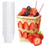 2a3bd3d856aa70227d574604d522e6f4jpg › Udanewypieki Clear plastic cup stack beside a fruit-filled layered dessert cup with strawberries, blueberries, watermelon, and pink straws