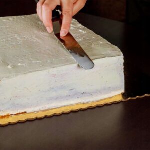 Person smooths gray frosting over a large rectangular cake with an offset spatula in hand.