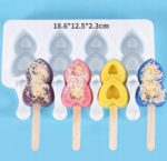 81b9b805ecfdc63d57573d951bc6212fjpg › Udanewypieki Row of four colorful, heart-shaped popsicles (purple, pink, yellow, blue) with coconut topping, set in a white silicone mold tray against a blue background.
