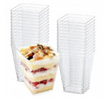 8849b10b58104b06ed66dc5abdcb04c7jpg › Udanewypieki Stackable clear plastic dessert cups with square bases, shown with layered fruit-and-cream parfait in one cup used for individual servings.