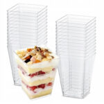 Stackable clear plastic dessert cups with square bases, shown with layered fruit-and-cream parfait in one cup used for individual servings.