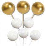 9b709fee4eaa81dd13ac064e9cf6020e-1jpg › Udanewypieki Close-up of gold and white spherical lollipops on sticks against a white background, arranged in a cluster.