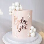 Side view of a pink cake decorated with white fondant pearls cascading down the edge and cursive text 'Baby' on the front.