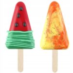 be2fcd07697160ad061af39d883f3c91jpg › Udanewypieki Two candy popsicles on sticks: a red cone with green swirls and black dots, and a yellow-orange marbled pop.